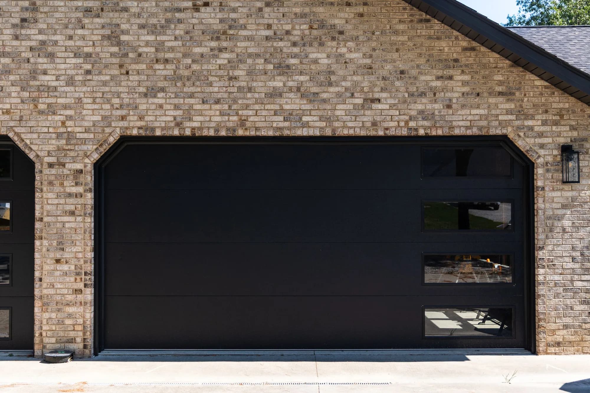 Black flush garage door with a vertical stack of windows on a tan brick garage