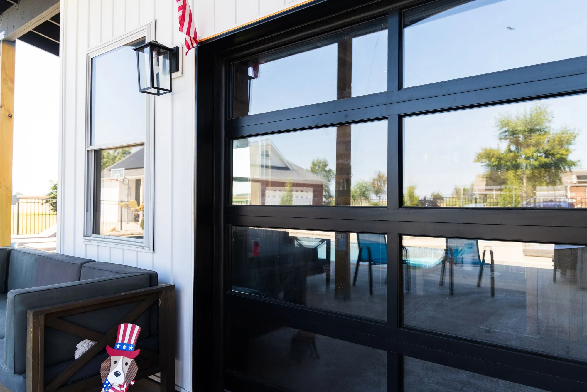 Black-framed full view glass garage door beside a covered patio on a white farmhouse
