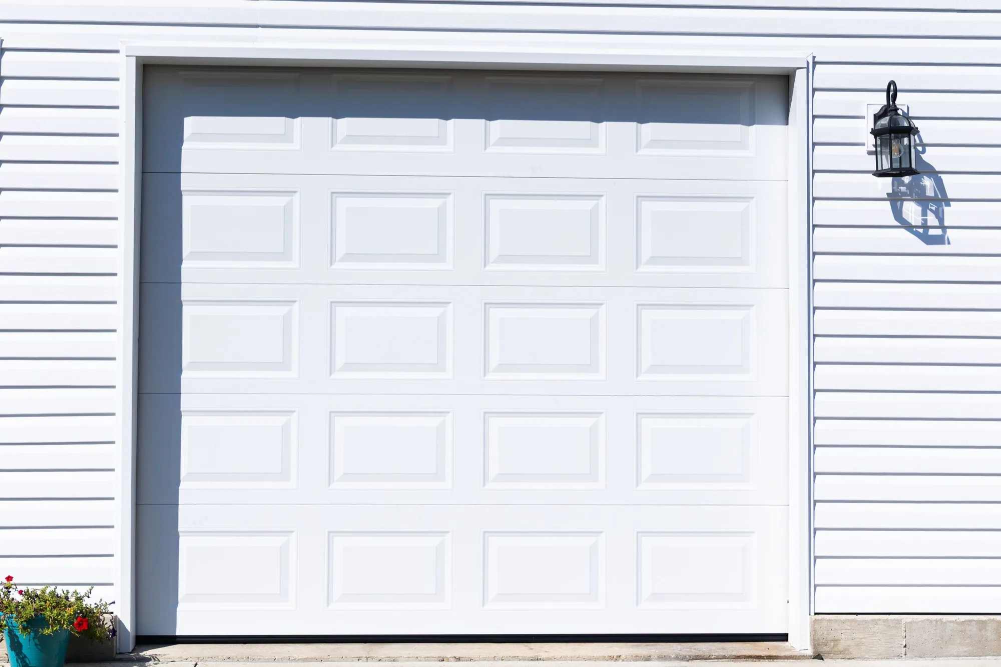 White short raised-panel garage door on a white vinyl-sided garage with a black coach lantern