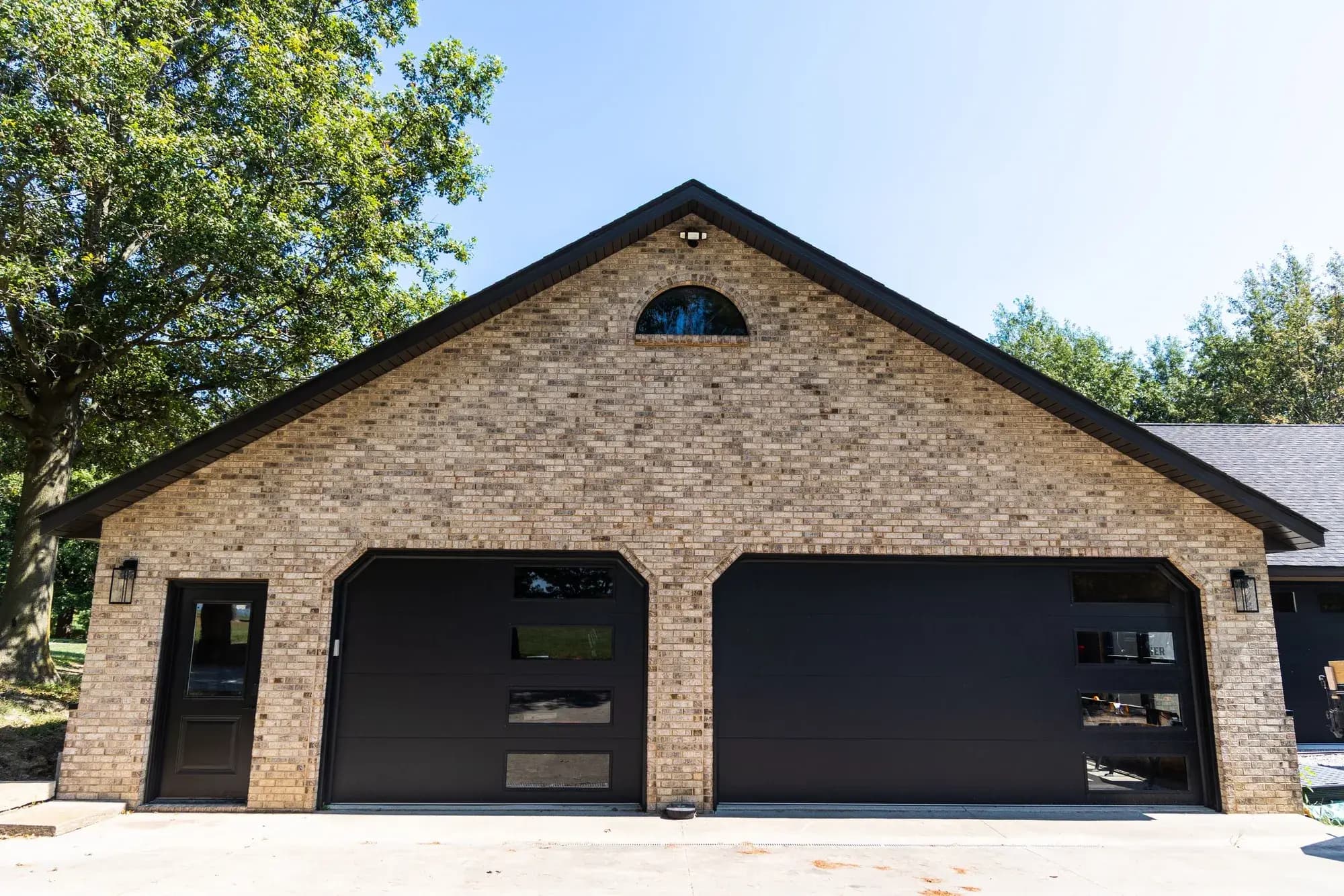 Two black flush garage doors with vertical window stacks on a tan brick garage