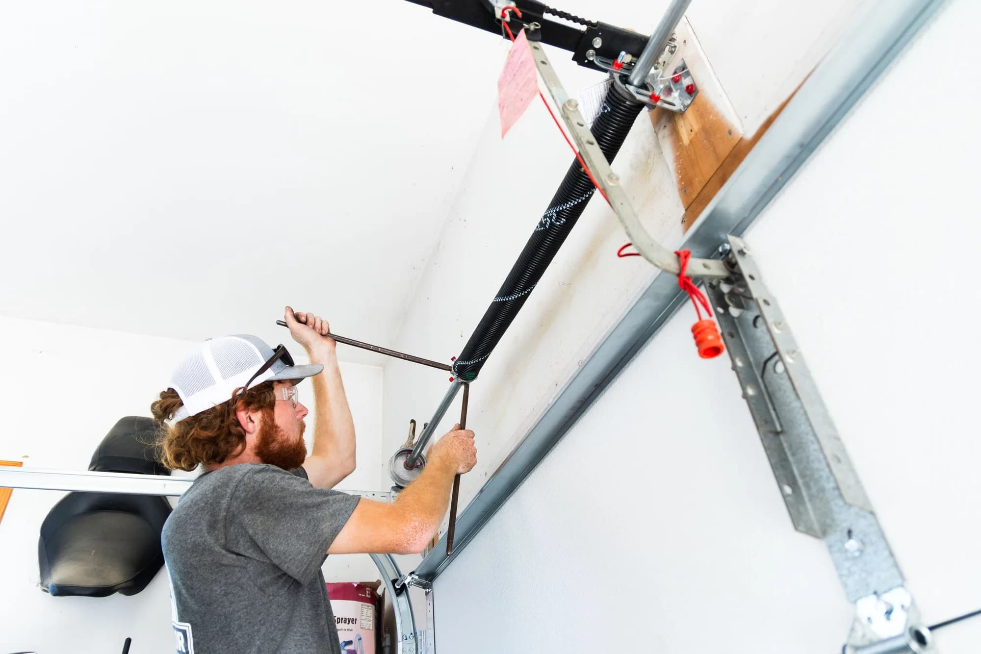 Technician winding a torsion spring above a garage door with winding bars